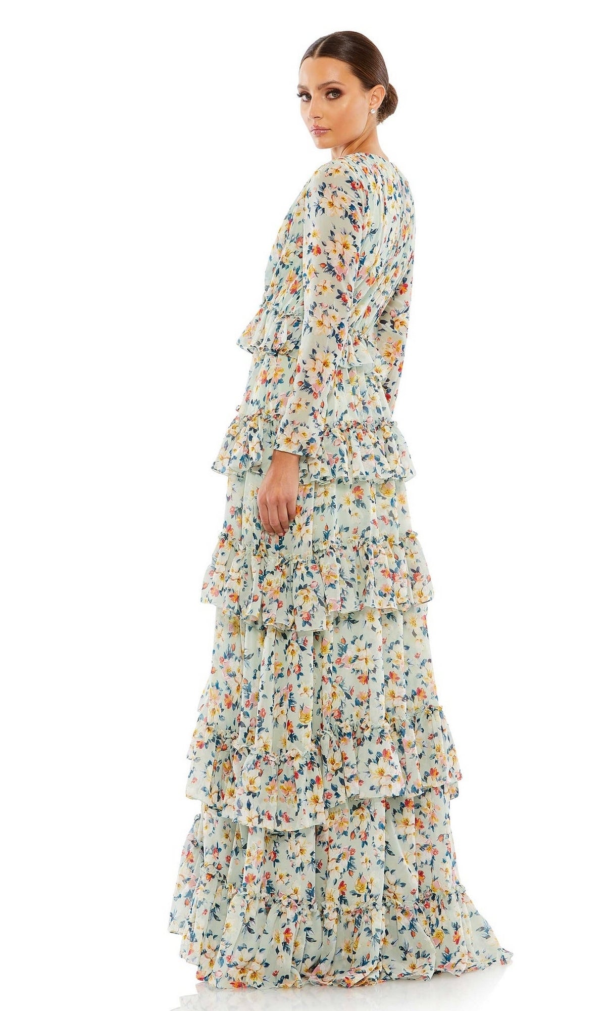 A woman faces away, wearing the Long Formal Dress 55664 by Mac Duggal—a floor-length gown with a light blue background, colorful floral print, and tiered ruffles.